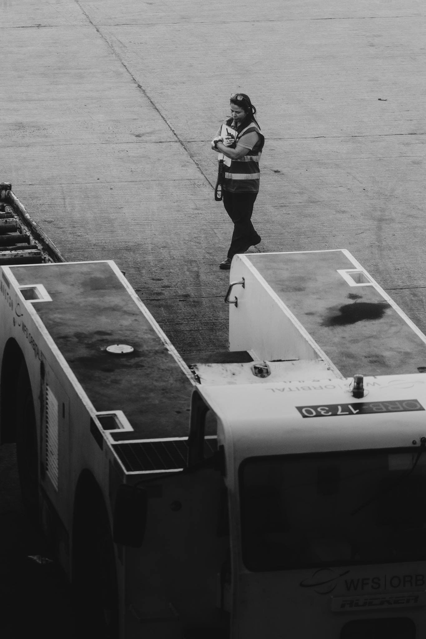 A ground crew member walking on the airport tarmac beside aircraft equipment.