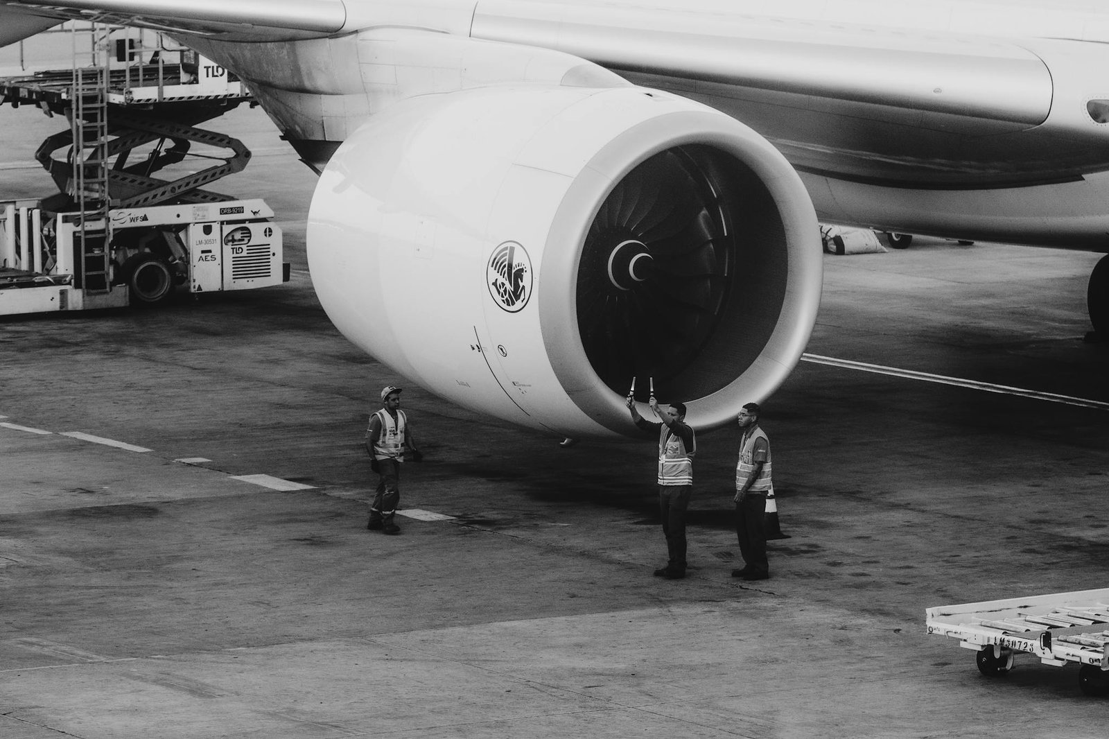 Black and white photo of aviation workers inspecting a jet engine on the tarmac.