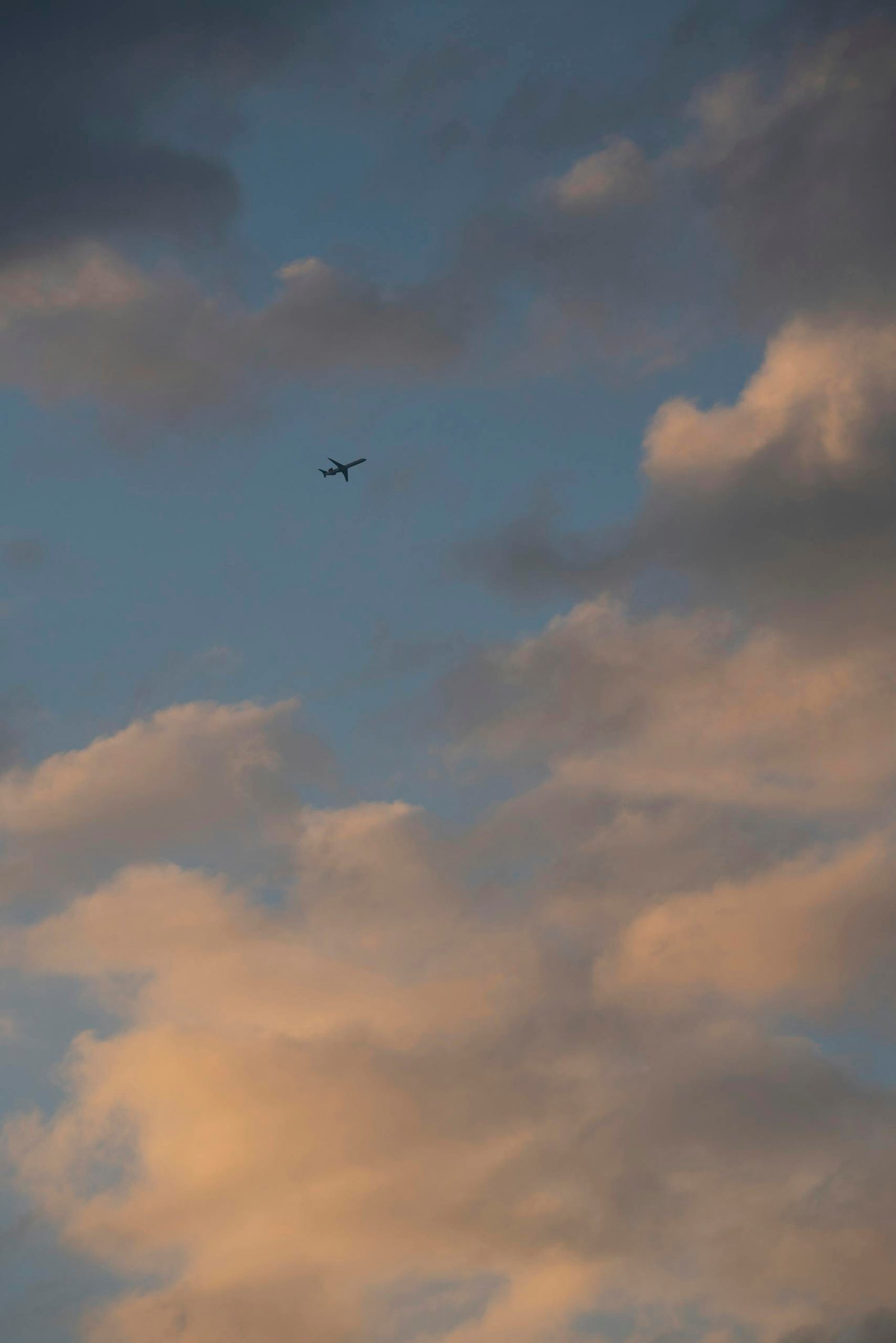 Silhouette of an airplane flying against a dramatic cloudy sunset sky.